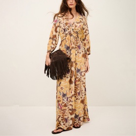 Model wearing Bash yellow ikat-print maxi dress with wide sleeves and tie waist, styled with brown fringed bag and flat sandals