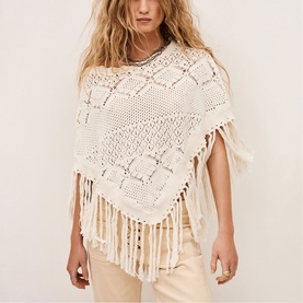 Model wearing Bash cream crochet poncho with fringe hem, styled with beige trousers and delicate necklace