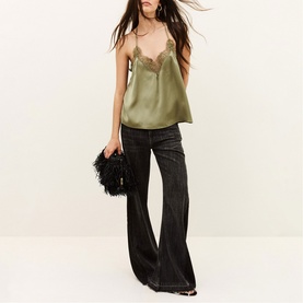 Model wearing Bash green satin cami top with lace trim, styled with black wide-leg jeans and carrying a black feathered clutch bag