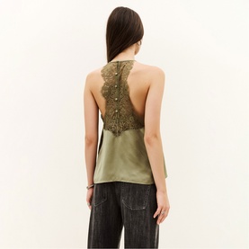 Model wearing Bash green satin halterneck top with lace open back panel, styled with dark wide-leg jeans