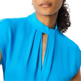Model wearing Whistles blue dress with pleat detail keyhole neckline and short sleeves, styled with small stud earrings.