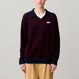 Model wearing Claude Pierlot black knit polo sweater with navy contrast collar and cuffs, styled with tan trousers