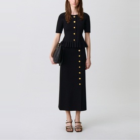 Model wearing Claude Pierlot black knit peplum top and midi skirt with gold buttons, styled with black strappy heels and clutch bag