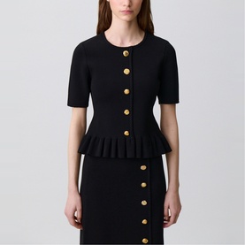 Model wearing Claude Pierlot black short-sleeve peplum cardigan with gold buttons, styled with matching black peplum skirt.