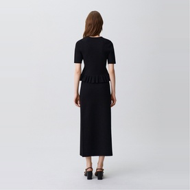 Model wearing Claude Pierlot black knit midi dress with peplum waist detail and short sleeves, viewed from behind, styled with black heeled sandals.