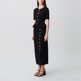 Model wearing Claude Pierlot black midi dress with gold buttons, peplum waist, short sleeves and front slit, styled with brown strappy sandals