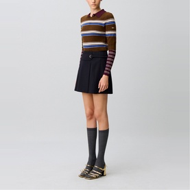 Model wearing Claude Pierlot black mini skirt with pleated detail, styled with multicolour stripe knit top, grey knee socks and gold flat sandals