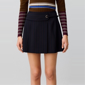 Model wearing Claude Pierlot black pleated mini skirt with gold-tone buckle detail, styled with a striped long-sleeve top.