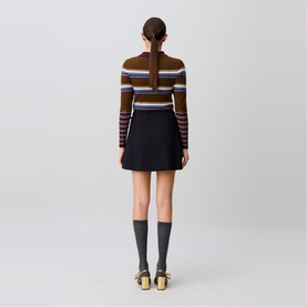 Model wearing Claude Pierlot black mini skirt with striped brown and blue ribbed knit top, grey knee-high socks and gold sandals, rear view.