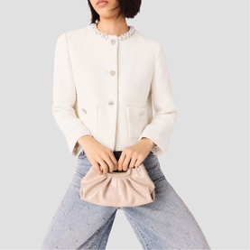 Model carrying Maje bag in mastic beige, styled with a white embellished jacket and blue jeans