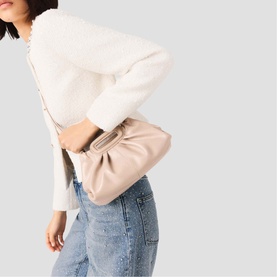 Model carrying Maje bag in mastic beige, styled with a cream knit top and light-wash jeans