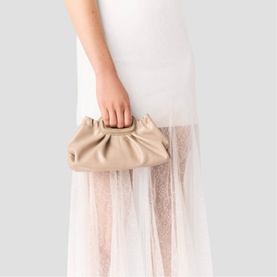 Model carrying Maje bag in mastic beige, ruched gathered clutch with top handle, styled with white tulle skirt