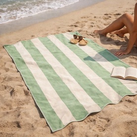 Allure Scallop Beach Towel Green with wide green and cream stripes laid on sand, styled with sandals, sunglasses and an open book.