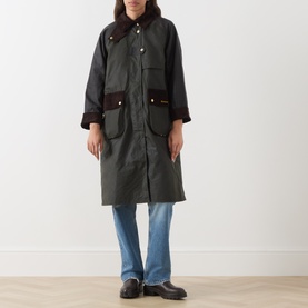 Model wearing Barbour Kirklees Wax Long Jacket in Fern, longline cut with corduroy collar and flap pockets, styled with blue jeans and loafers