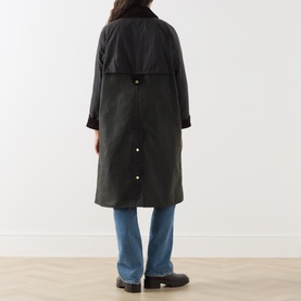 Model wearing Barbour Kirklees Wax Long Jacket in Fern, longline cut with corduroy collar and snap buttons, styled with blue jeans, back view.