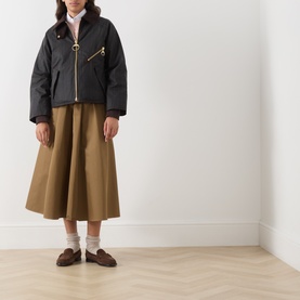 Model wearing Barbour waxed cotton jacket in Shadow Classic, styled with olive midi skirt and brown loafers