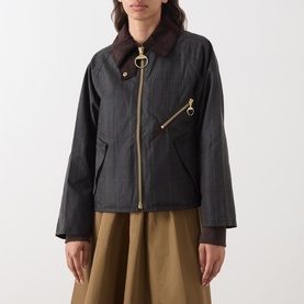 Model wearing Barbour waxed cotton jacket in Shadow Classic, brown corduroy collar, gold ring zip detail, styled with khaki skirt