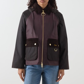 Model wearing Barbour wax cotton jacket in Rustic/Bordeaux/Muted colourblock with gold zip, snap pockets, and contrast sleeves, styled with blue
