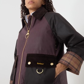 Model wearing Barbour wax cotton jacket in Rustic/Bordeaux/Muted with gold zip, corduroy pocket, and tartan lining detail.