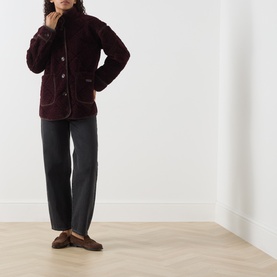 Model wearing Barbour Maplewood Fleece Jacket in Fig/Ganache with contrast trim, styled with grey wide-leg trousers and brown loafers