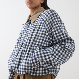 Model wearing Barbour gingham navy and neutral quilted bomber jacket with tan collar, styled with khaki trousers.
