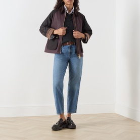 Model wearing Barbour mid blue straight-leg jeans with brown belt, styled with dark gilet, white shirt and black loafers.