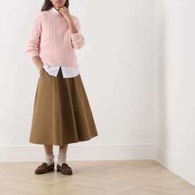 Model wearing Barbour Ashdown Cable-Knit Sweater in Pink Blush, styled with white shirt, khaki midi skirt and brown loafers.