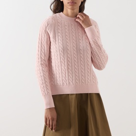 Model wearing Barbour Ashdown Cable-Knit Sweater in Pink Blush, featuring cable-knit pattern and round neck, styled with an olive midi skirt.