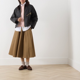 Model wearing Barbour Ashdown Cable-Knit Sweater in Pink Blush, styled with black jacket, tan midi skirt and brown loafers.