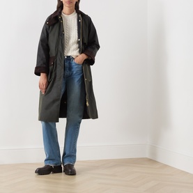 Model wearing Barbour Ashdown Cable-Knit Sweater in Ecru, styled with dark wax jacket, blue wide-leg jeans and black loafers.