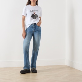 Model wearing Barbour Mariana Dog T-Shirt in white with dog photo print, styled with mid-blue straight-leg jeans and black chunky shoes.