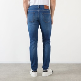 Model wearing Dolce & Gabbana Straight Leg Jeans in mid blue with faded details and logo badge, styled with white trainers. Rear view.