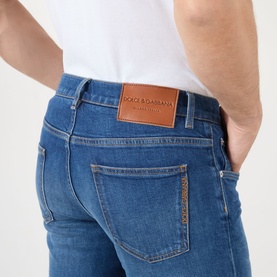 Model wearing Dolce & Gabbana Straight Leg Jeans in mid blue denim, showing tan leather logo badge on back pocket, styled with white T-shirt.