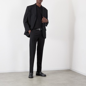 Model wearing Dolce & Gabbana black cotton jeans, styled with a matching black blazer, polo shirt, and leather shoes.