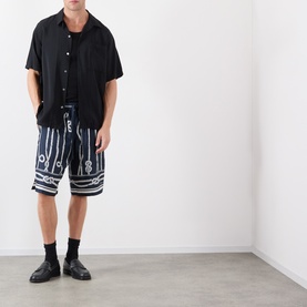 Model wearing Dolce & Gabbana navy silk shorts with white rope print, styled with black short-sleeve shirt and black loafers.