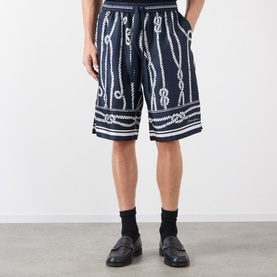 Model wearing Dolce & Gabbana navy silk shorts with all-over rope-knot print, styled with black socks and loafers.