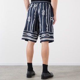 Model wearing Dolce & Gabbana navy silk shorts with all-over white rope and knot print, styled with black socks and black shoes.