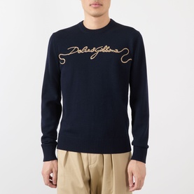 Model wearing Dolce & Gabbana dark blue wool sweatshirt with embroidered cursive logo, styled with beige trousers.