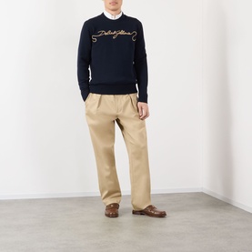 Model wearing Dolce & Gabbana dark blue wool sweatshirt with script logo, styled with white shirt, beige trousers and brown loafers.