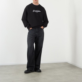 Model wearing Dolce & Gabbana black Logo Graphic Sweatshirt with crew neck and contrast logo, styled with dark wide-leg jeans and black shoes.