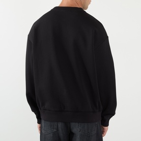 Model wearing Dolce & Gabbana Logo Graphic Sweatshirt in black, crew neck, dropped shoulders, ribbed trims. Styled with dark jeans. Rear view.