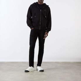 Model wearing Dolce & Gabbana black Logo Plate Hoodie with zip fastening and drawstring hood, styled with black jeans and white trainers.