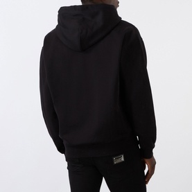 Model wearing Dolce & Gabbana Logo Plate Hoodie in black, rear view showing hood with drawstring, paired with black trousers.