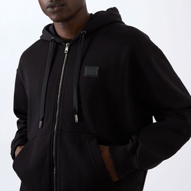 Model wearing Dolce & Gabbana Logo Plate Hoodie in black, showing zip fastening, drawstring hood, and chest logo plate detail.