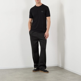 Model wearing Dolce & Gabbana black Logo Badge T-Shirt with round neck, styled with black straight-leg trousers and dark trainers.