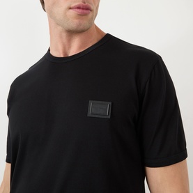 Model wearing Dolce & Gabbana Logo Badge T-Shirt in black, with tonal leather logo badge at chest, round neckline and short sleeves.