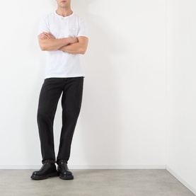 Model wearing Dolce & Gabbana Logo Badge T-Shirt in Optical White with black slim trousers and black leather shoes.