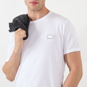 Model wearing Dolce & Gabbana Logo Badge T-Shirt in Optical White with chest logo badge, styled with a dark denim jacket over shoulder.