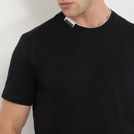 Model wearing Dolce & Gabbana Logo Tab T-Shirt in black, featuring contrasting crew neck and silver logo tab detail at neckline.