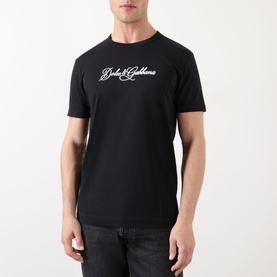 Model wearing Dolce & Gabbana Script Logo T-Shirt in black with white script branding, round neckline and short sleeves, styled with dark jeans